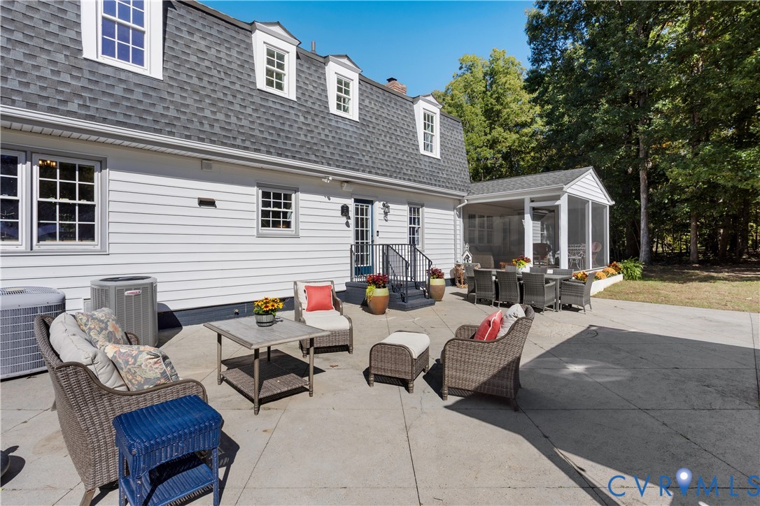 Concrete patio featuring an attached screened-in porch, white horizontal siding, multiple dormer windows, and a shingled gambrel roof