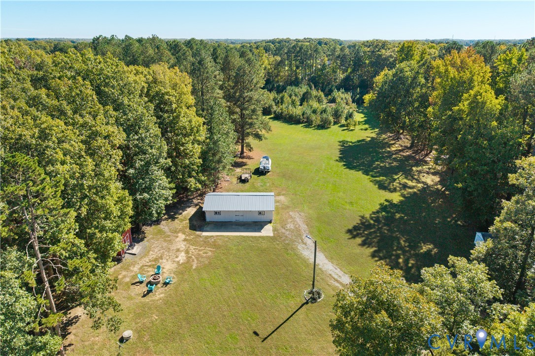Expansive acreage featuring mature perimeter trees, an open grass field, and a detached metal-roofed structure with a concrete pad