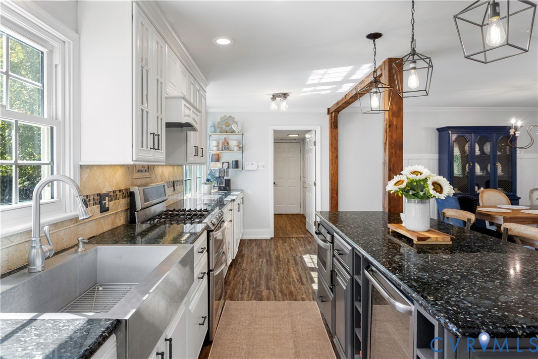 Kitchen featuring a farmhouse-style sink, dark stone countertops, custom cabinetry, wood-finish flooring, and exposed wooden support beam with geometric pendant lighting