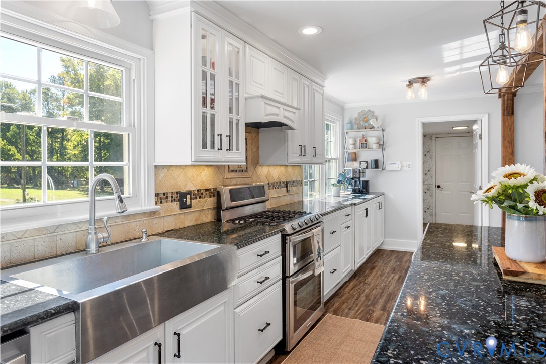 Kitchen featuring white cabinetry, stainless steel farmhouse sink, stone countertops, wood-finish flooring, and industrial-style pendant lighting