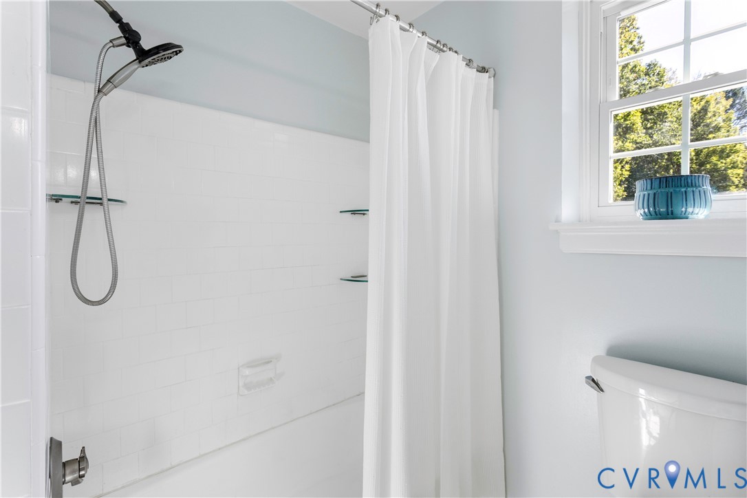 Shower area featuring white subway tile surround, built-in glass shelving, multi-function shower head, and a double-hung window