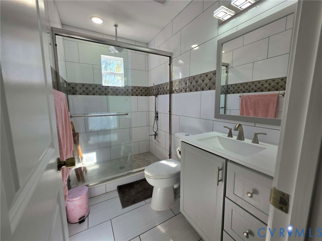 Full hallway bathroom featuring lovely ceramic tile work, a walk-in shower, modern lighting, and a gray vanity with sink.