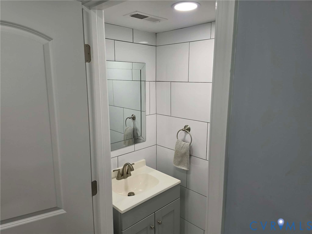 Downstairs Half bath featuring a gray vanity with sink, toilet and ceramic tile throughout.