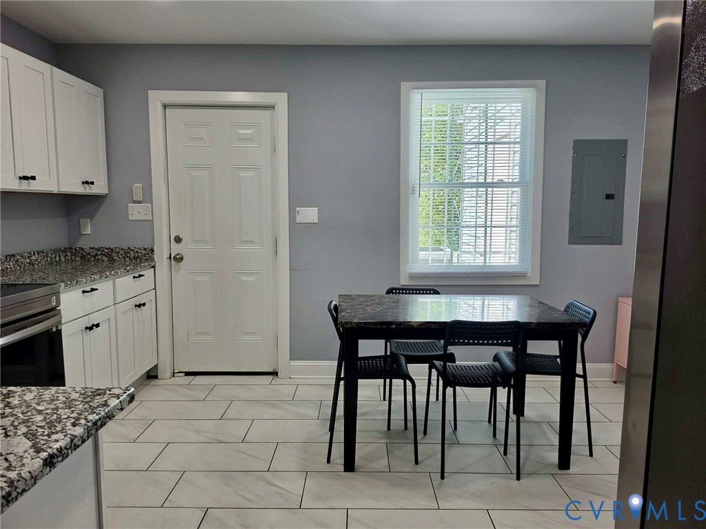 Eat-in style kitchen featuring granite countertops, ceramic tile, stainless steel appliances, white cabinets with matte black pulls & a stack, washer and dryer.