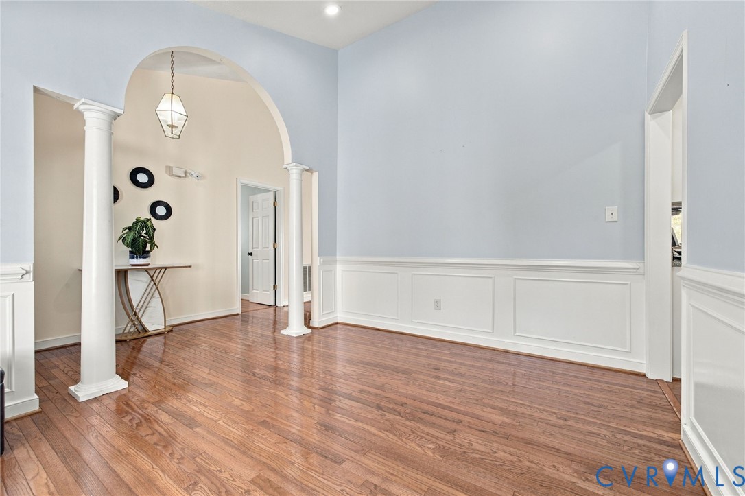 Dining Area, High ceilings featuring an arched opening with columns, hardwood flooring, and wainscoting detailing Dining Area, High ceilings featuring an arched opening with columns, hardwood flooring, and wainscoting detailing