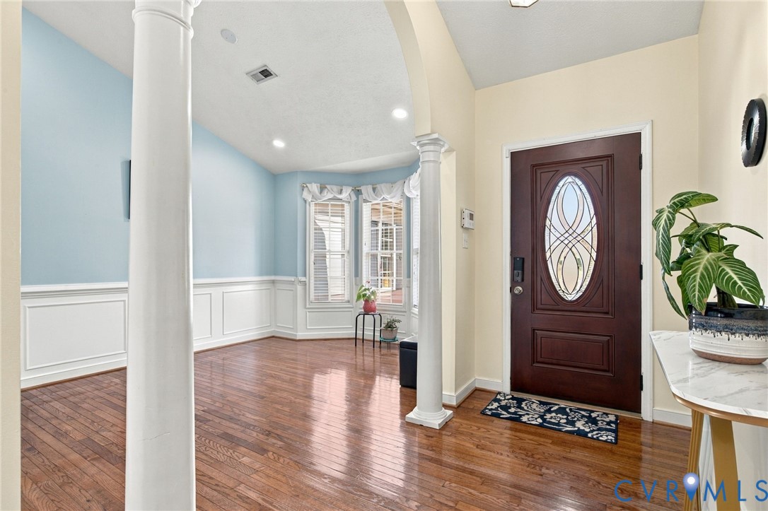 Entryway featuring hardwood flooring, classic architectural columns, arched entry, wainscoting, and a decorative glass-insert entry door Entryway featuring hardwood flooring, classic architectural columns, arched entry, wainscoting, and a decorative glass-insert entry door