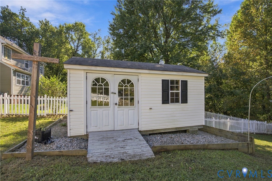 Detached storage shed featuring vinyl siding, dual-arched glass-paneled doors, shuttered window, and gravel-based hardscaping