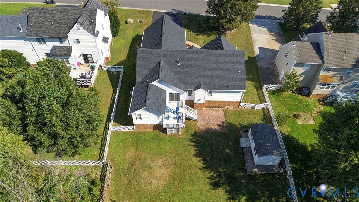 Aerial perspective of property featuring a multi-level asphalt shingle roof, brick and siding exterior, raised deck, brick patio, and fenced backyard