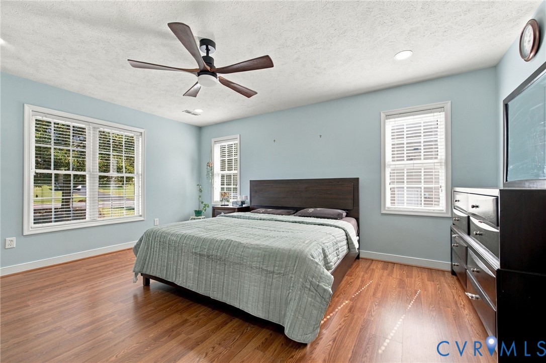 Primary bedroom featuring wood-finish flooring, recessed lighting, a five-blade ceiling fan, and multi-pane windows with horizontal blinds