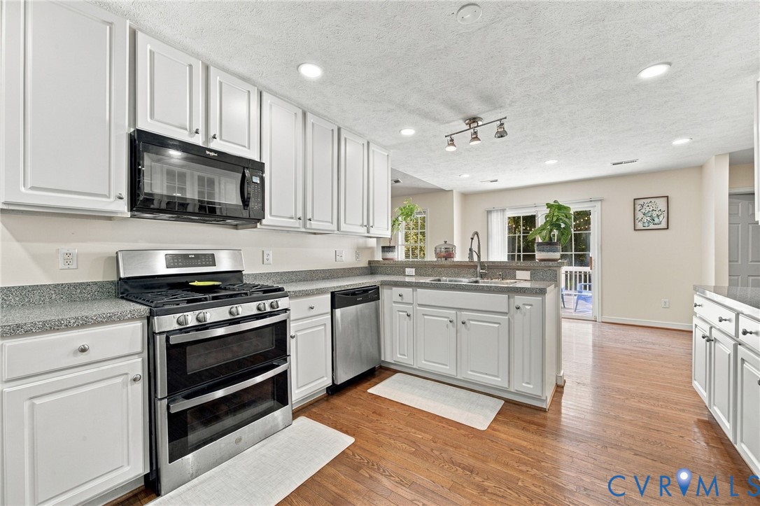 Kitchen featuring white shaker-style cabinetry, speckled stone-finish countertops, stainless steel appliance suite, wood-finish flooring, and recessed ceiling lighting Kitchen featuring white shaker-style cabinetry, speckled stone-finish countertops, stainless steel appliance suite, wood-finish flooring, and recessed ceiling lighting