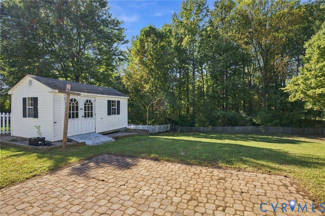 Backyard featuring a paved stone patio, white vinyl picket fencing, and a detached outbuilding with double-door entry