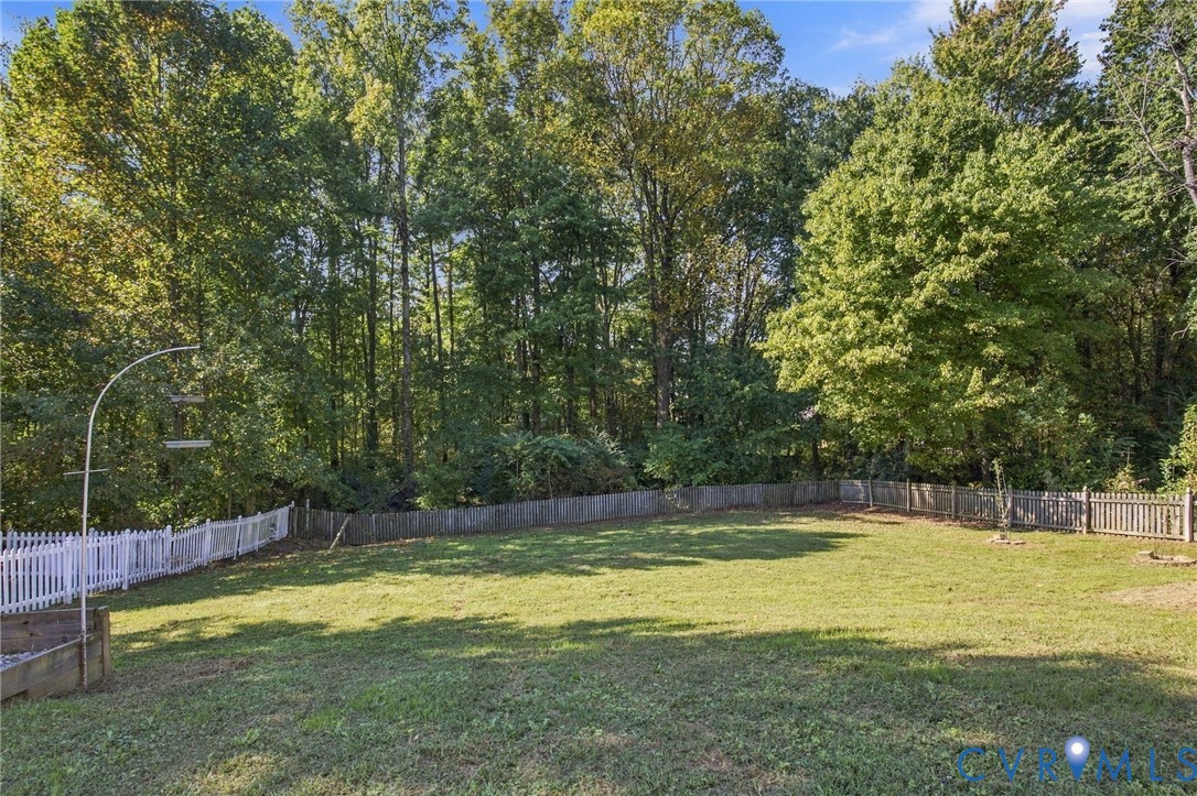 Expansive backyard featuring a level lawn, white picket fencing, wood-slat perimeter fencing, and mature trees