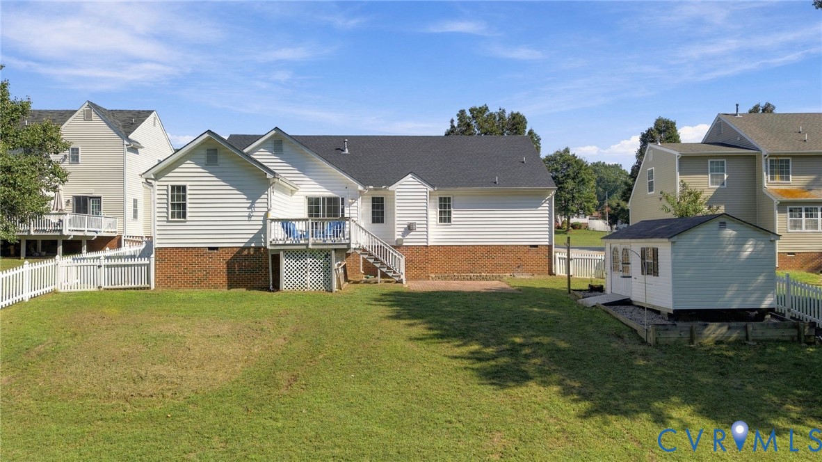 Backyard featuring a vinyl siding exterior with brick foundation, an elevated deck with lattice skirting, a detached storage shed, and a perimeter picket fence