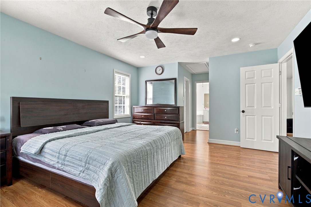 Primary bedroom with Wood-finish flooring, ceiling fan with integrated lighting, multi-panel interior door, recessed lighting, and single-hung window with colonial grid pattern