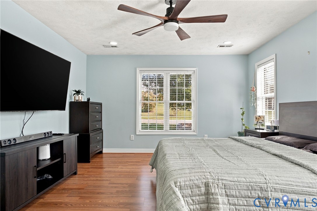 Primary bedroom featuring wood-finish flooring, a multi-blade ceiling fan with integrated lighting, and dual windows equipped with white shutter blinds