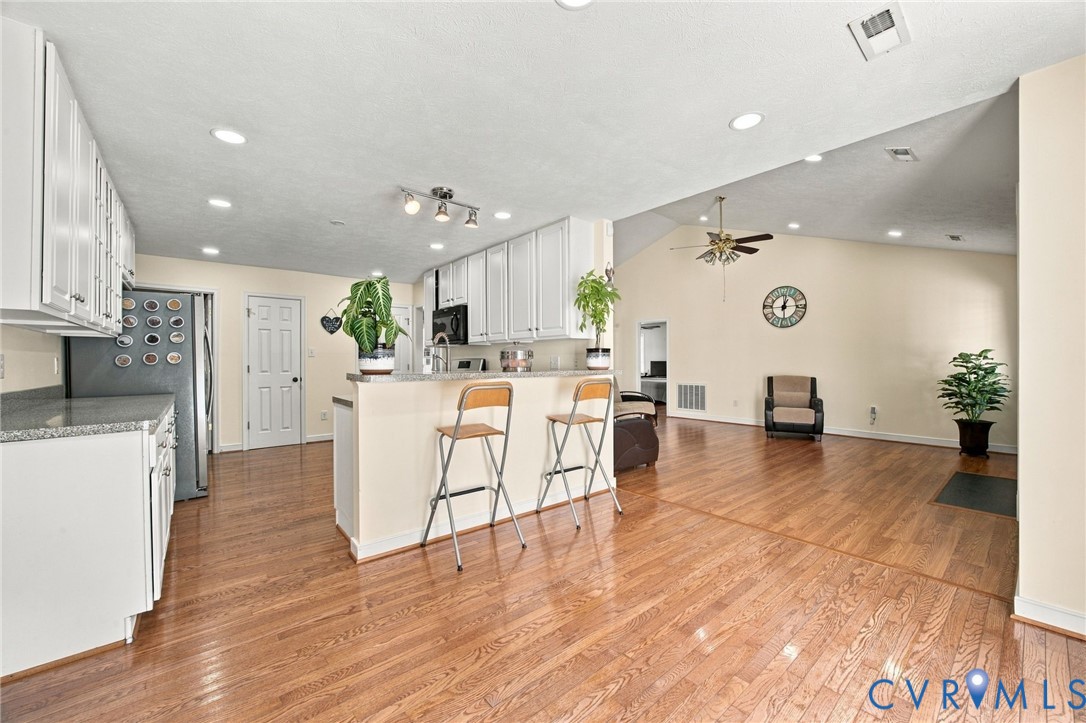 Kitchen featuring white shaker-style cabinetry, solid-surface countertops, recessed lighting, and wood-finish flooring with vaulted ceilings Kitchen featuring white shaker-style cabinetry, solid-surface countertops, recessed lighting, and wood-finish flooring with vaulted ceilings