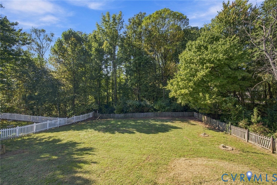 Expansive backyard featuring a level lawn, white picket fencing, wood-slat perimeter fencing, and mature trees