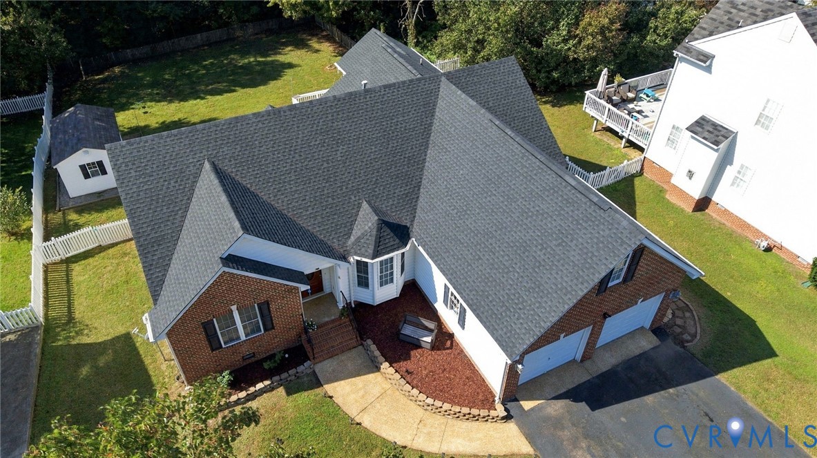 Aerial perspective of a multi-gabled brick and siding residence featuring a two-car garage, asphalt shingle roof, curved hardscape walkway, and an external storage structure