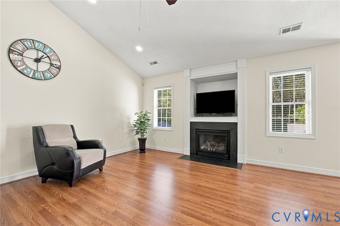 Living room with Vaulted ceilings, wood-finish flooring, built-in entertainment niche, and fireplace with black surround
