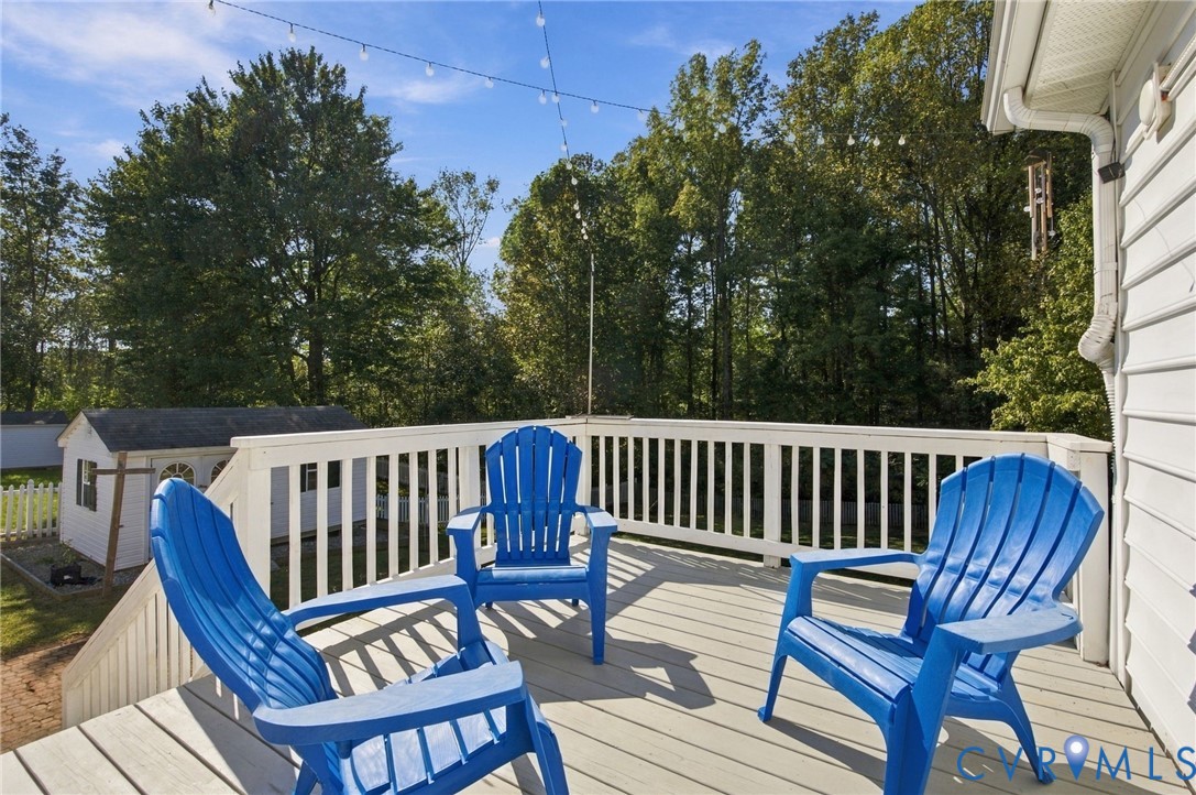 Elevated wooden deck featuring white railing and string lighting, overlooking a private backyard with a storage shed