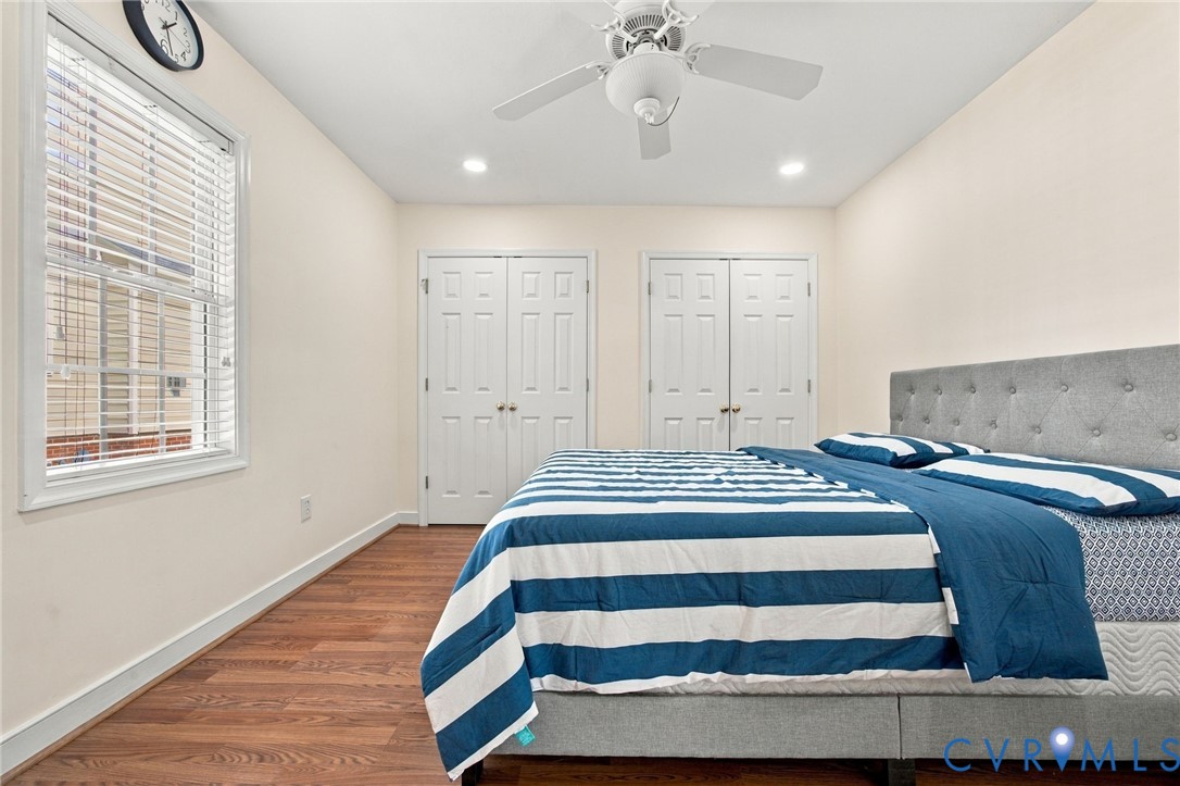 Bedroom with Wood-finish flooring, dual sets of double-panel closet doors, recessed lighting, and a white ceiling fan with integrated light fixture