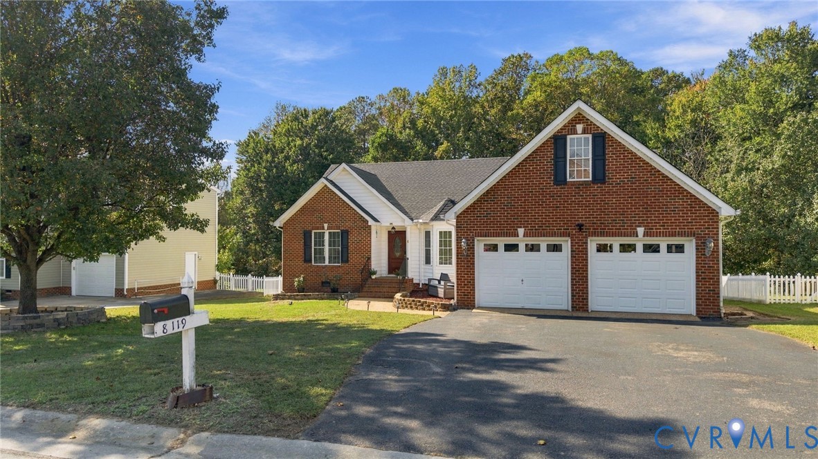 Brick exterior featuring a two-car garage, asphalt driveway, covered entryway, and white picket fencing