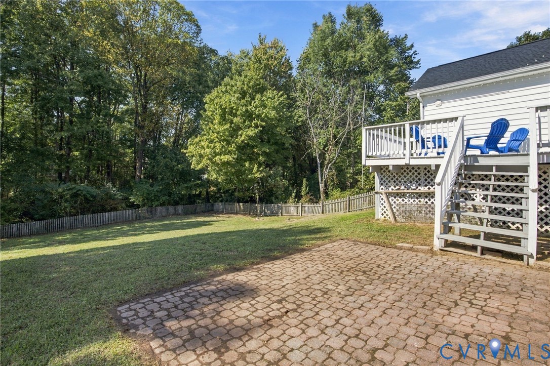 Backyard featuring a stone paver patio, elevated deck with railing, lattice under-deck skirting, and wood-fenced perimeter