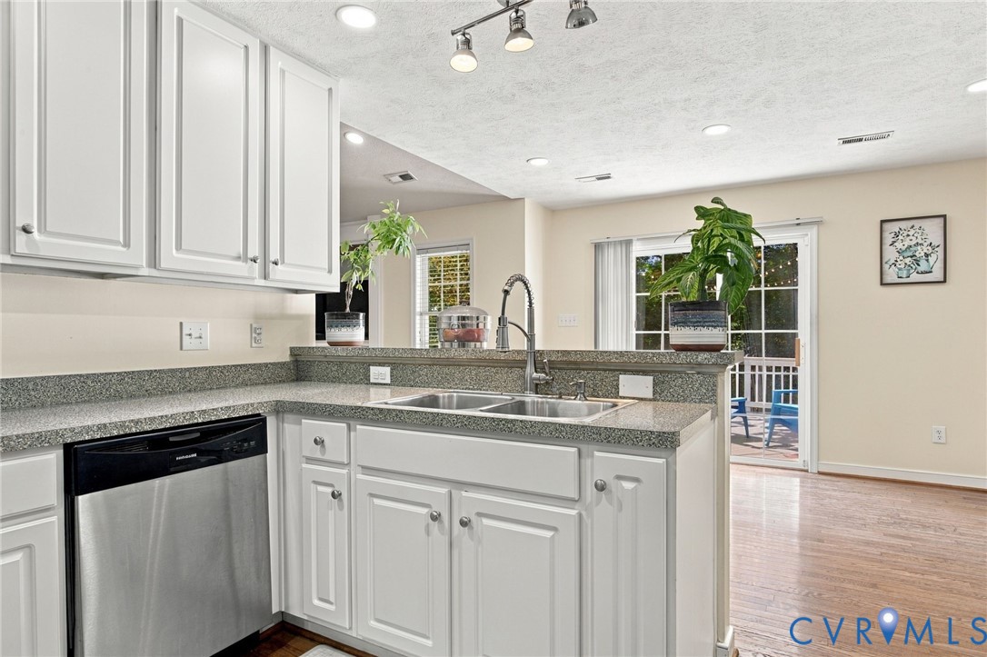 Kitchen featuring white cabinetry, stone-finish countertops, a stainless steel dishwasher, a dual-basin stainless steel sink with a high-arch faucet, and wood-finish flooring Kitchen featuring white cabinetry, stone-finish countertops, a stainless steel dishwasher, a dual-basin stainless steel sink with a high-arch faucet, and wood-finish flooring