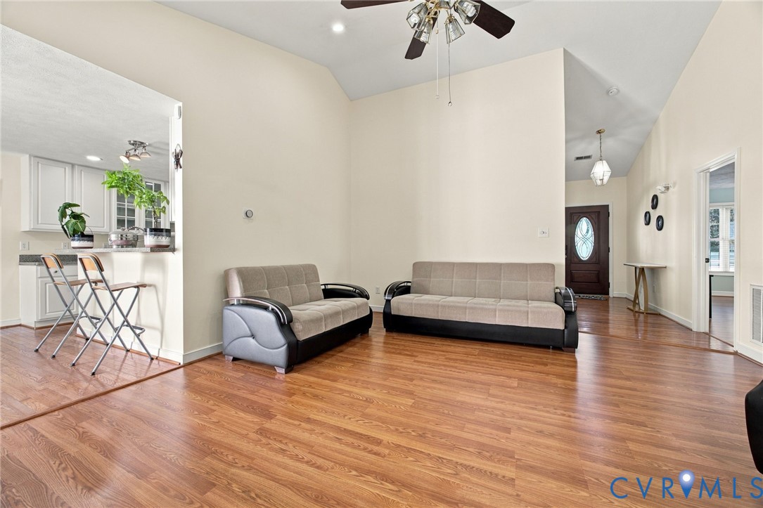 Living Room with Vaulted ceilings featuring a multi-blade ceiling fan, wood-finish flooring, and a pass-through opening to the kitchen area