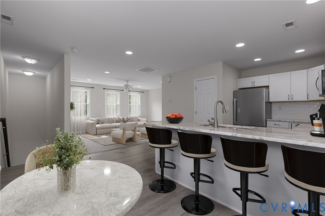 Kitchen featuring stone-patterned countertops, a breakfast bar, recessed lighting, white cabinetry, and stainless steel appliances, set against wood-finish flooring