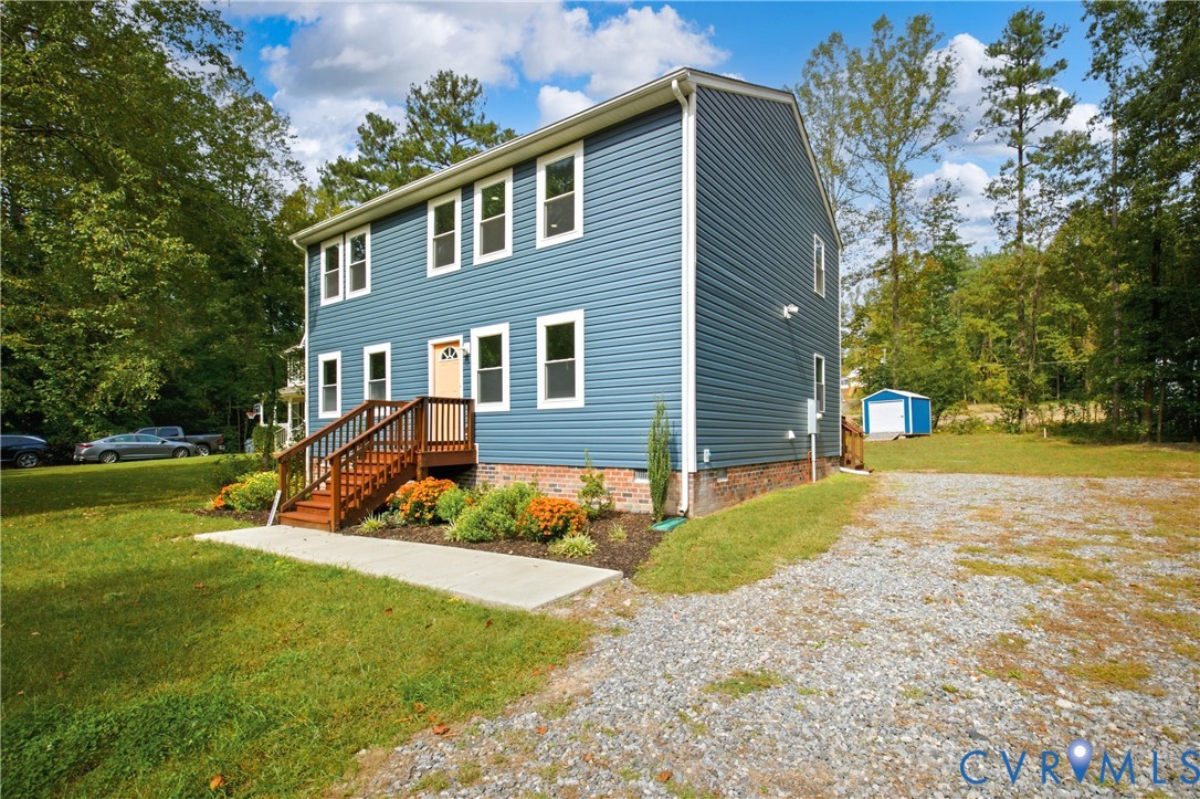 Two-story home with blue vinyl siding, brick foundation, wood-framed exterior staircase, concrete walkway, and gravel driveway