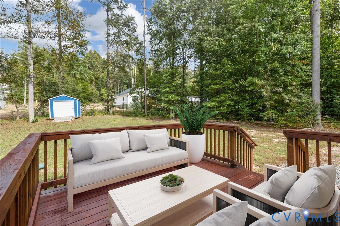Elevated wooden deck with balustrade railings overlooking a partially wooded lot featuring a detached storage structure