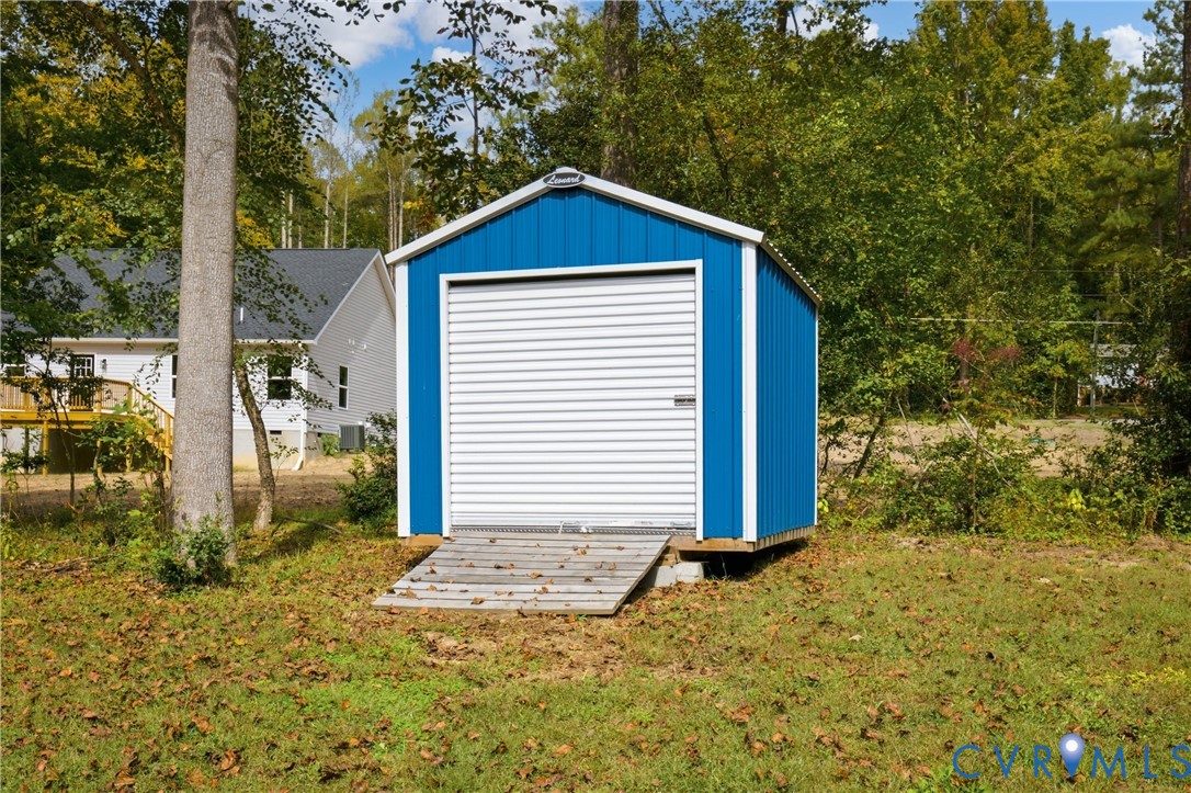 Detached storage structure featuring metal siding, a white roll-up door, and an integrated wood-slat ramp