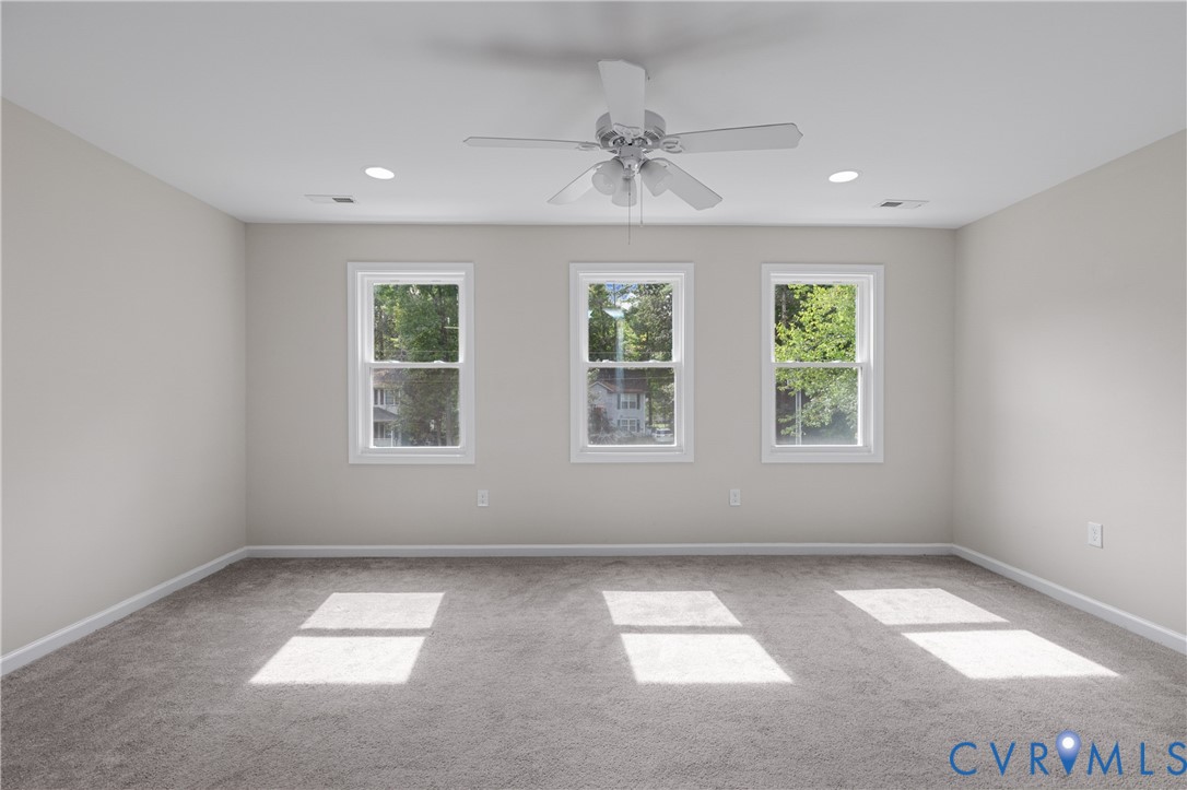 Neutral wall palette, carpeted flooring, triple window configuration, and overhead ceiling fan with integrated lighting