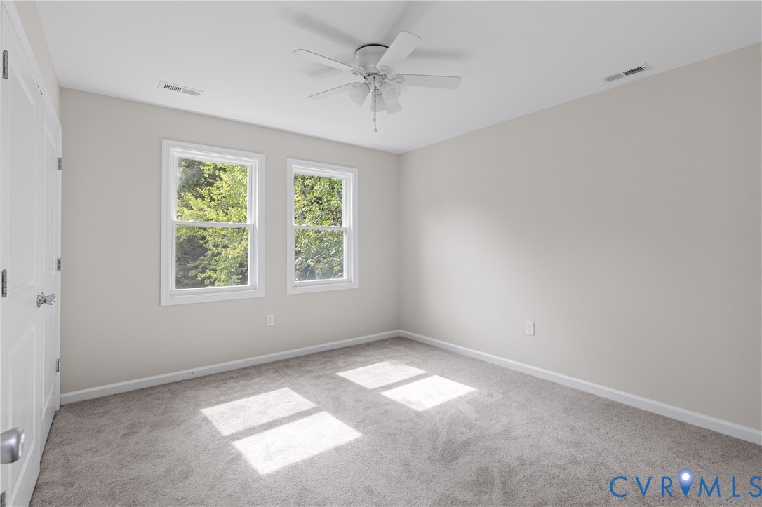 Neutral interior space featuring carpeting, white walls, dual-pane windows, and a ceiling fan with integrated light fixture