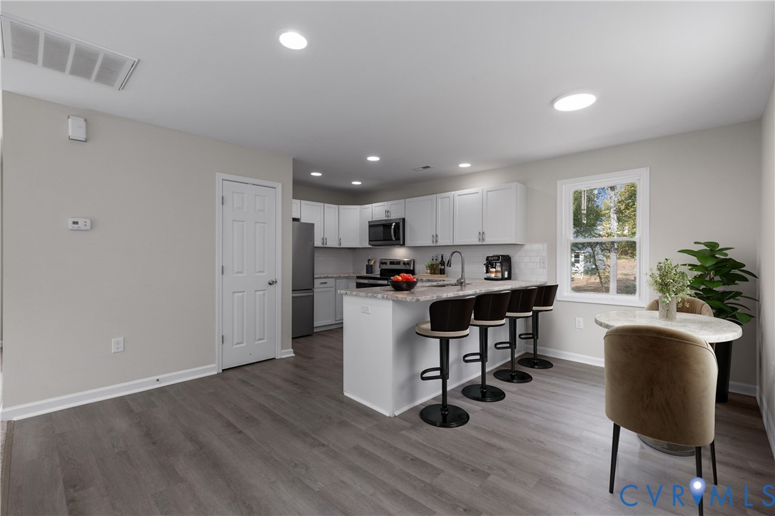 Kitchen featuring white shaker-style cabinetry, stone-patterned countertops, a peninsula with seating, stainless steel appliances, and wood-finish flooring