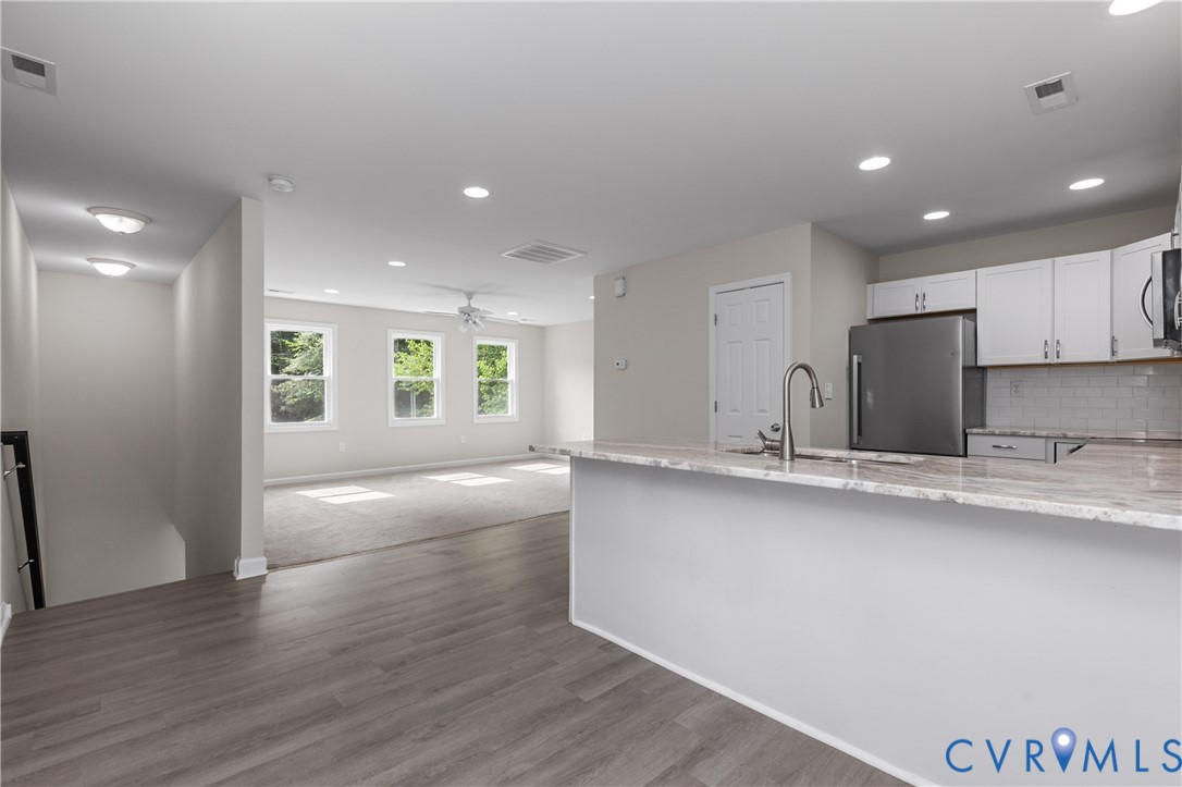 Kitchen featuring stone-finish countertops, stainless steel refrigerator, white cabinetry, tile backsplash, and recessed lighting