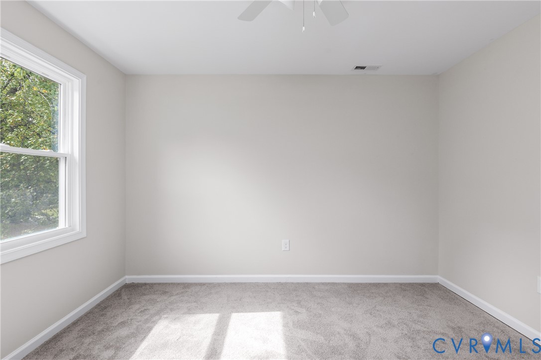 Neutral-toned interior space featuring wall-to-wall carpeting, a single-hung window, and a ceiling-mounted fan