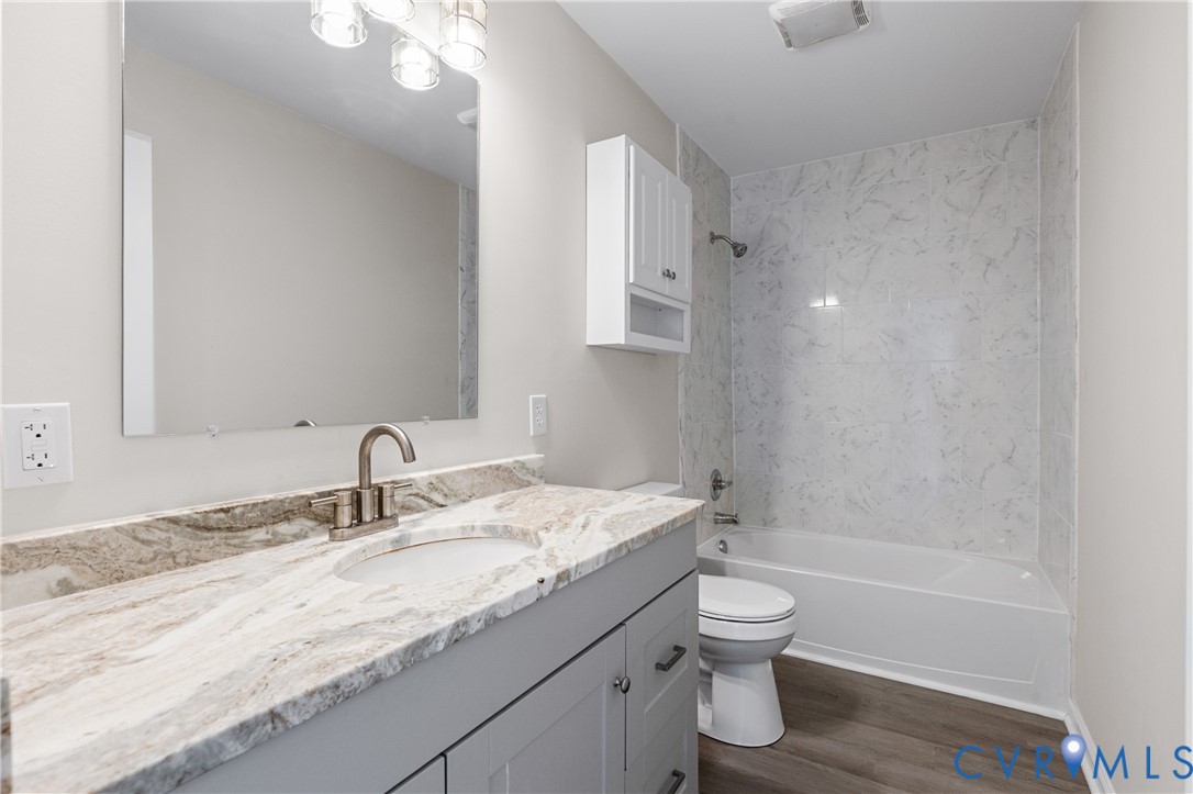 Bathroom featuring a grey vanity with stone countertop, an integrated sink, a large wall-mounted mirror, and a tub-shower combination with surround tile