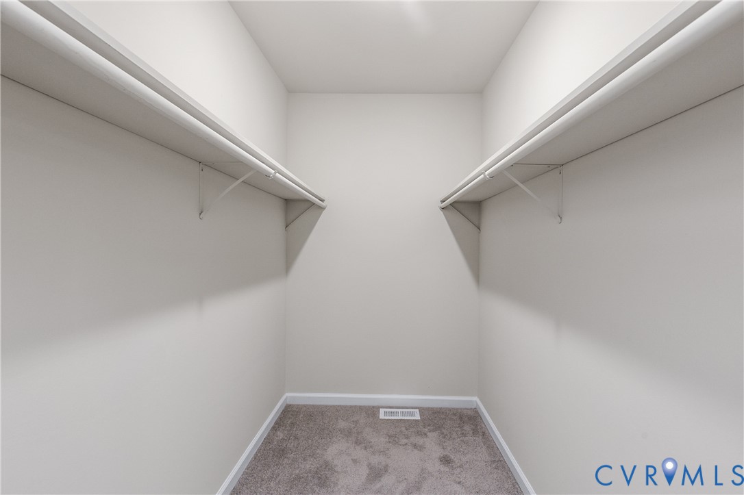 Walk-in storage space featuring neutral carpeting and dual-sided built-in shelving with integrated rods