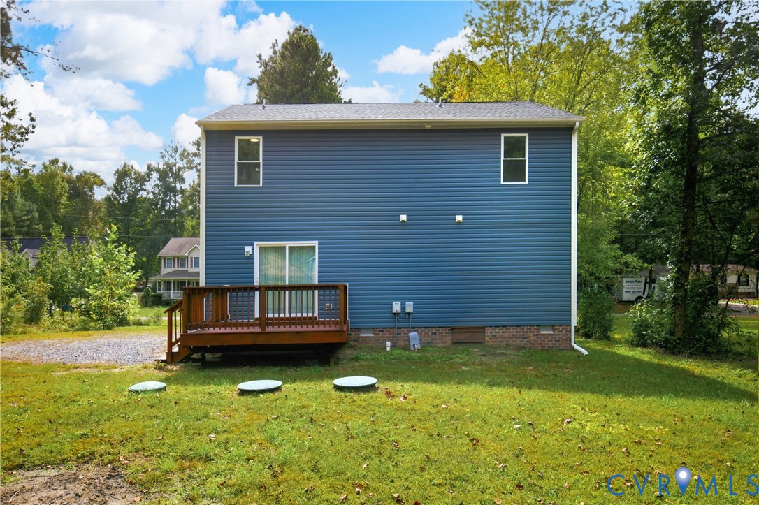 Rear exterior featuring blue horizontal siding, a raised wood deck, a brick foundation base, and a sliding glass door