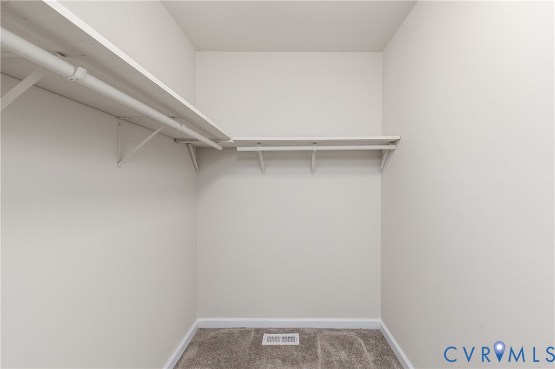 Walk-in storage space featuring neutral wall paint, wall-to-wall carpeting, and wrap-around shelving with integrated garment rods