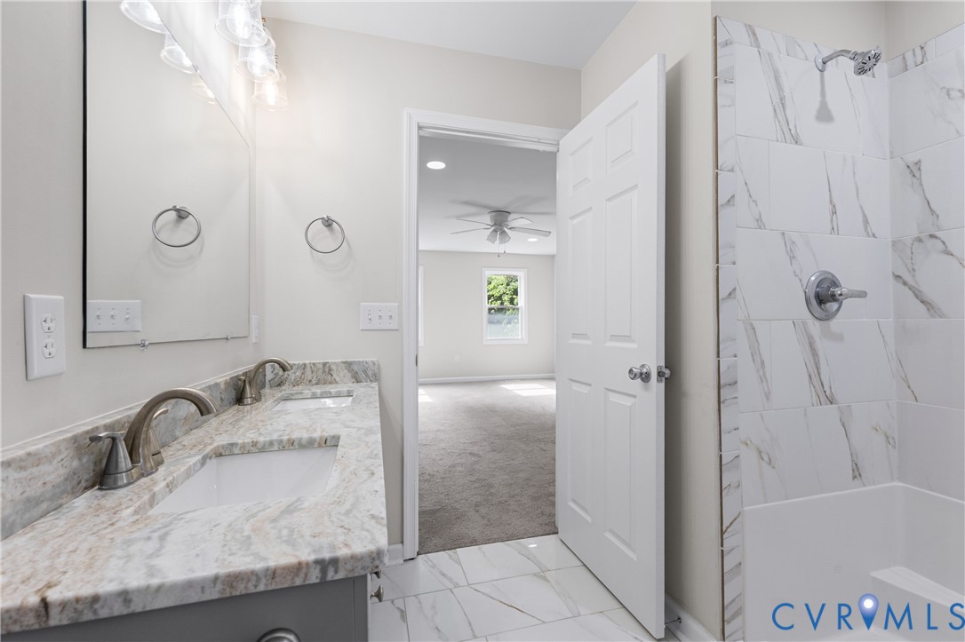 Bathroom featuring a dual-sink vanity with stone-finish countertop, undermount sinks, large wall-mounted mirror, and a shower-tub combination with tiled surround