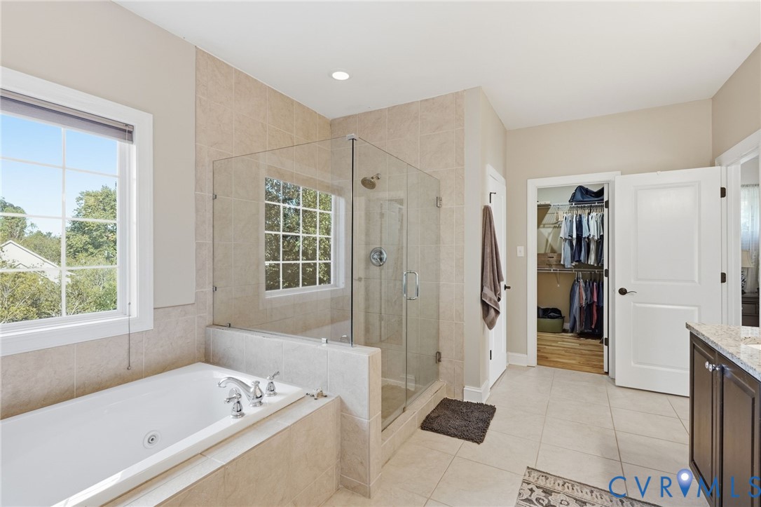 Bathroom featuring a soaking tub, glass-enclosed walk-in shower with tile surround, stone-top vanity, and walk-in closet