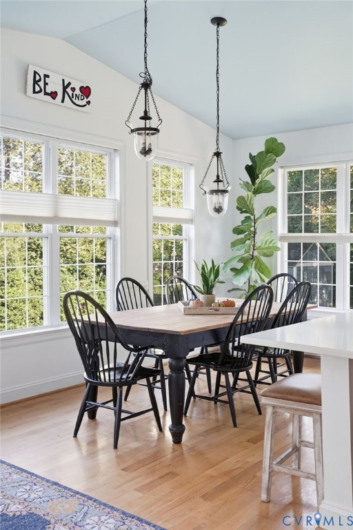 Dining area featuring vaulted ceilings with light blue accent paint, wood-finish flooring, and multiple windows with white grids