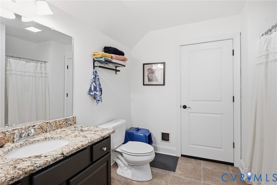 Dark-finished vanity with a stone-top integrated sink, large wall-mounted mirror, ceramic tile flooring, and a two-panel interior door