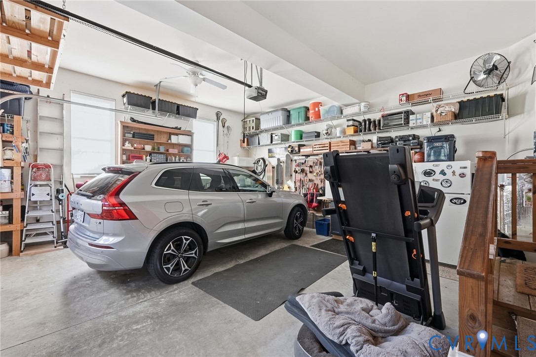 Attached garage featuring concrete flooring, overhead storage shelving, integrated wall-mounted wire shelving units, and a wooden staircase