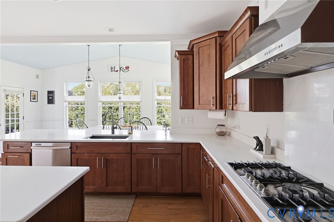 Kitchen featuring custom wood cabinetry, expansive stone countertops, stainless steel gas cooktop with a professional-style range hood, integrated dishwasher, and wood-finish flooring
