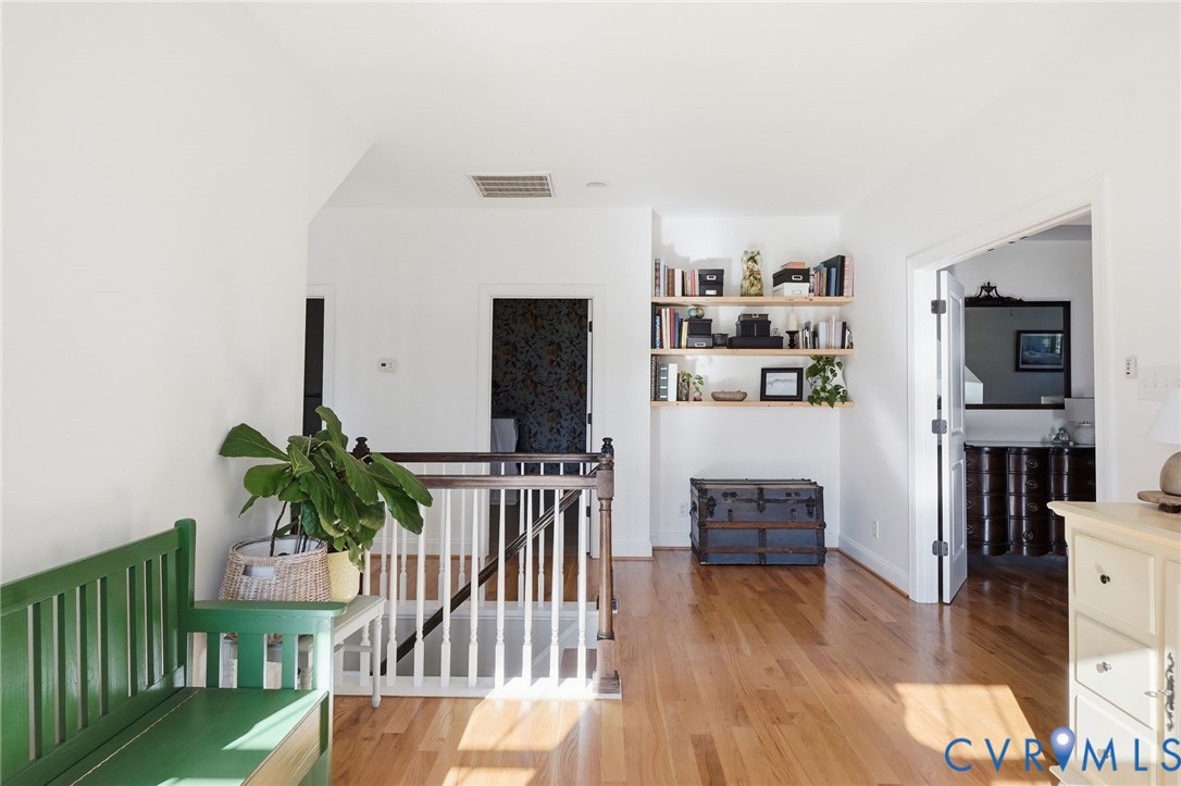 Hardwood flooring, wood-finish railing with white balusters, and built-in wall shelving