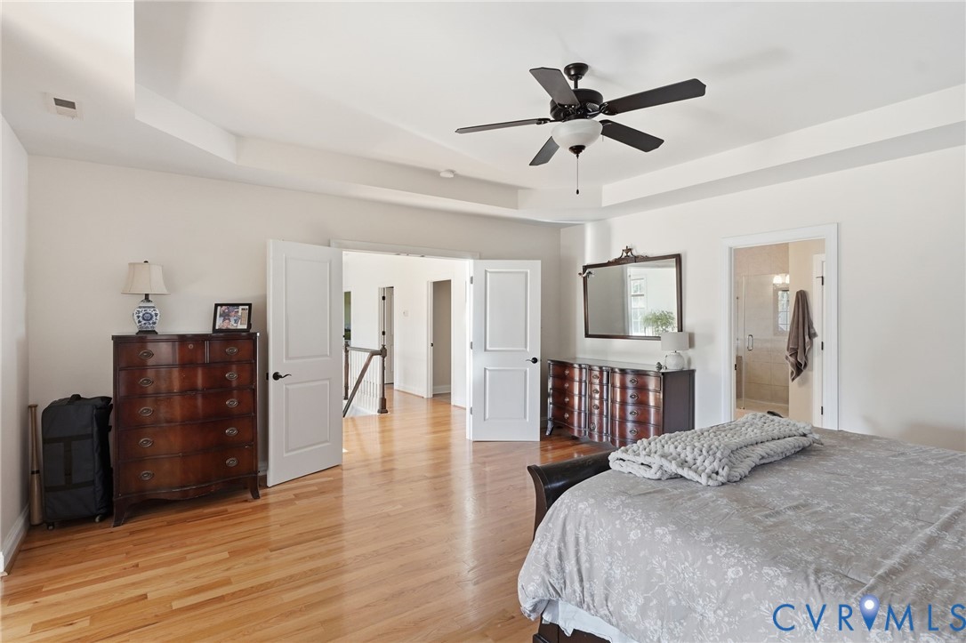 Tray ceiling featuring a central matte black ceiling fan, wood-finish flooring, and multi-panel interior doors